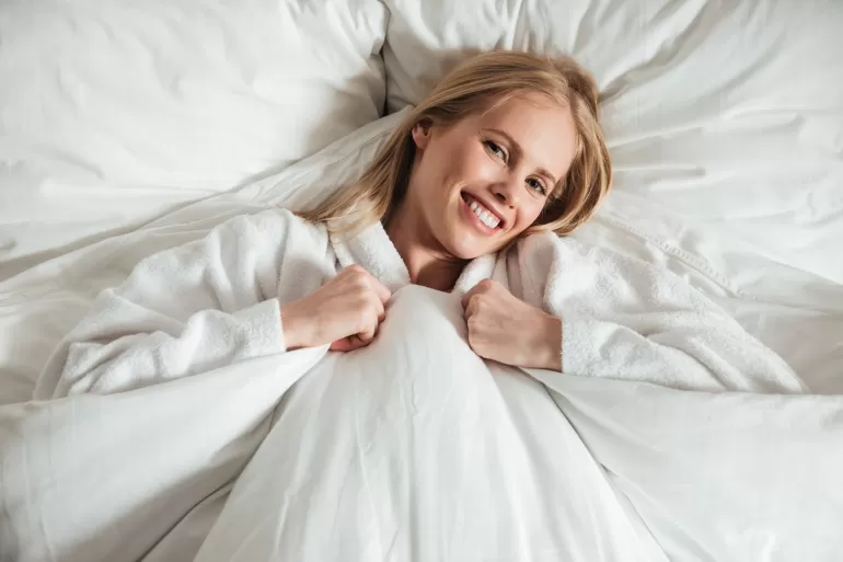 young happy woman lying big white bed with blanket