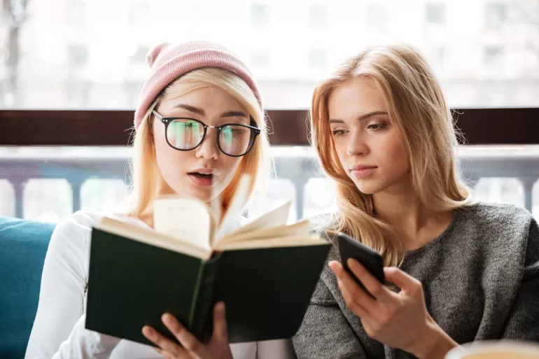 cheerful two women friends sitting cafe reading book