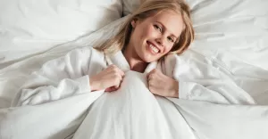 young happy woman lying big white bed with blanket